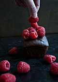 A woman placing a raspberry on top of a chocolate cake topped with raspberries