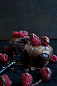 A chocolate cake topped with raspberries and melted milk chocolate, cut in half, with raspberries and a knife on a black countertop