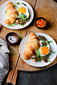 A croissant sandwich with fried eggs and mushrooms