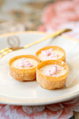 Mini tarts filled with cream and pink meringues on a glass plate