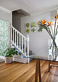 Vase of flowers on glass table and foot of staircase in foyer with whitewashed brick wall