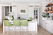 White center block with green bar stools, fitted wardrobes and copper pots in an open kitchen