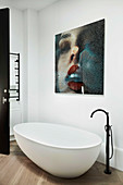 Frei stehende Badewanne mit Standarmatur und moderne Kunst an der Wand im Bad