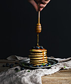 Pancake tower with fresh blueberry and mint, hand is keeping wooden stick pouring honey flow