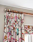 Brightly patterned curtain draped in elegant folds with matching roller blind
