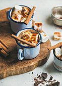 Hot chocolate in enamel mugs with cinnamon and roasted marshmallows