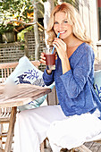 Blonde Frau in blauem Shirt und weißer Hose mit einem Drink