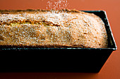 A loaf cake being dusted with icing sugar