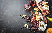 A platter of cheese, meat, crackers, bread, grapes and nuts with red wine
