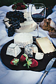 A cheese platter with strawberries and red wine on a picnic blanket