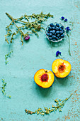 Stillleben mit Pfirsich, Blaubeeren und Trockenblumen auf pastellblauem Untergrund