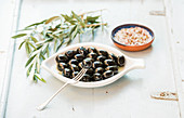 Schwarze Oliven auf weißem Keramikteller mit Zweigen und Gewürzen
