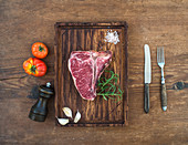 Rohes T-Bone-Steak mit Knoblauchzehen, Tomaten, Rosmarin und Salz
