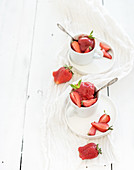 Strawberry sorbet ice-cream with mint leaves in cups over rustic white wooden background