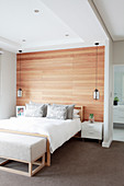 Doppelbett vor Holzverkledung, Nachtkasten und Pendelleuchte in elegantem Schlafzimmer