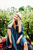 A blonde woman wearing a blue summer dress sitting on a tractor