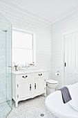 Washstand with countertop sink below window, toilet and free-standing bathtub in white bathroom