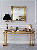 Tischlampe auf Konsole mit goldfarbenem Gestell und Glasplatte, darüber Wandspiegel mit Goldrahmen