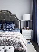 Doppelbett mit Bettkopfteil an hellgrauer Wand und elegantes Nachtkästchen mit Tischleuchte