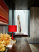 View over wooden table onto bench in alcove, wooden artwork in background