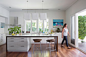 Kitchen island and bar stool in open kitchen with terrace access, woman in the background
