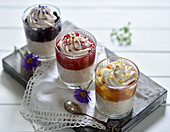 Vegan rice pudding desserts in glasses with apricot-mango, raspberry-rhubarb, and blueberry sauce decorated with coconut cream and flowers