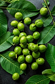 Green walnuts and walnut leaves on a black surface