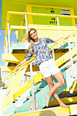 Blonde Frau in Shorts und geblümter Tunika steht an Strandhaus