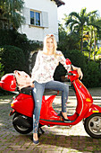 Blonde Frau in Jeans und Shirt sitzt auf Motorroller