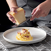 Parmesan wird über Spaghetti Carbonara gerieben