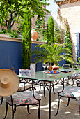 Metal outdoor furniture, palms and cypresses on terrace with blue screen wall