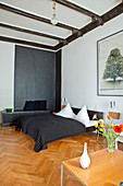 Double bed with black bedspread and low sideboard against black wall in bedroom