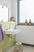 Waschbecken an grün gefliester Wand und Hocker im Badezimmer