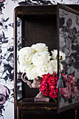 White ranunculus and a bouquet of red roses in a display case