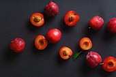 Rote süße Kirschpflaumen auf dunklem Hintergrund, ganz und halbiert