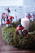 Candle lantern in moss wreath decorated with pine cones and toadstool ornaments