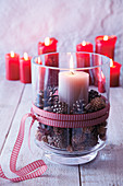 Festive arrangement of pillar candle and pine cones in glass vase on table