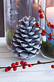 Pine cone, twigs and red berries in front of candle lanterns