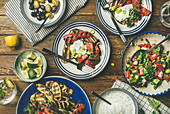 Healthy vegan dinner table setting - Fresh salad, grilled vegetables with yogurt sauce, pickled olives, lemon water