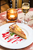 Ein Stück Käsekuchen auf Desertteller, Dessertwein und Kerze im Hintergrund