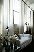 Weißes Sofa vor Backsteinwand mit Fabrikfenstern und langen Gardinen