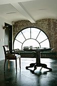 Old leather chair at pedestal table in front of large arched window