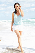 A brunette woman on a beach wearing shorts and a vest top