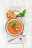 Cold tomato gazpacho soup in bowl with ice, hot pepper, basil and bread slices