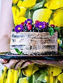 Frau im gelben Kleid hält Kuchen mit Traubenkirschen, Himbeeren und Blumen