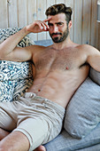 A young topless man lying on a sofa wearing shorts
