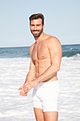 A young topless man on a beach wearing shorts