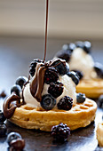 A waffle topped with ice cream and frozen berries being drizzled with melted chocolate