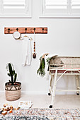 Coat rack on wall above potted cactus, wicker cot and wooden toys on floor
