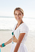 Blonde Frau in weißem Bolero und Rock mit Stickerei am Strand